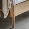 close up on footboard of light oak bed with natural throw thrown slightly over the end and slim feet on grey floor
