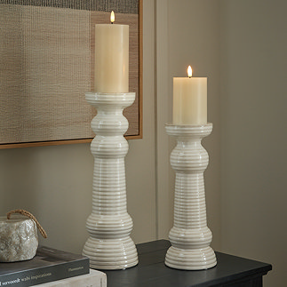 image of two ribbed ceramic pillar candles standing on a sideboard, containing battery-operated candles