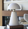 image of a light grey matt table lamp with dome shade, on top of a large book on a table