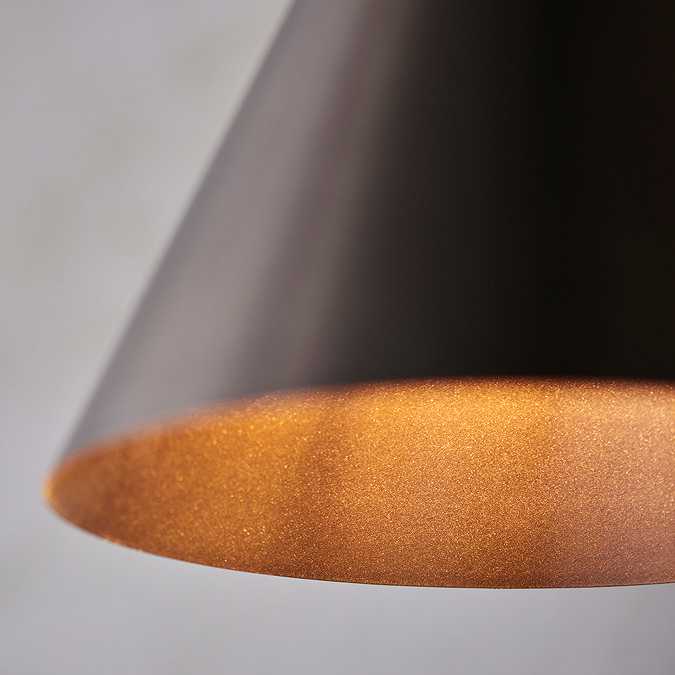 close up on bronze colour of conical ceiling light with warm glow of inside shade
