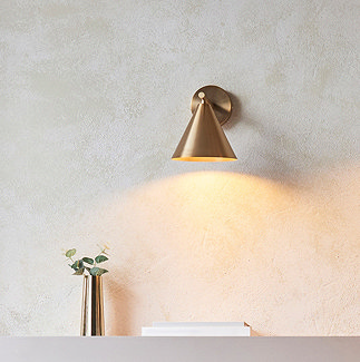 image of brass coloured wall light above a living room shelf, emitting warm glow onto thin faux plant