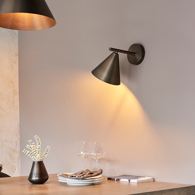 closer image of conical bronze wall light shining warm light onto dining table