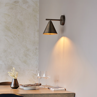 closer image of conical bronze wall light shining warm light onto dining table