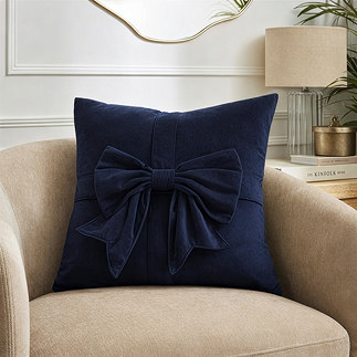 image of square navy blue cushion with a bow on its front, sat on cream armchair