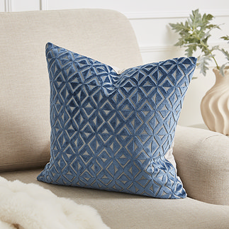 image of square cushion with blue and cream diamond pattern on the front, sat on a cream sofa