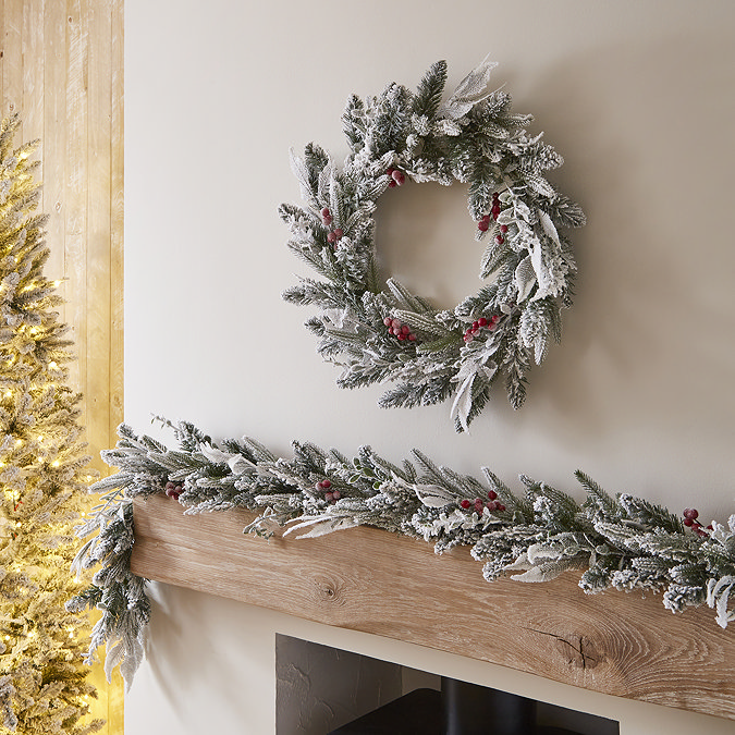 snow and berries wreath hung above a mantlepiece, with matching garland displayed along the mantlepiece below.