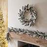 snow and berries wreath hung above a mantlepiece, with matching garland displayed along the mantlepiece below.