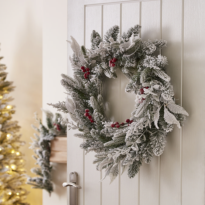 snow-dusted green wreath with red berries, hung on the back of a white living room door