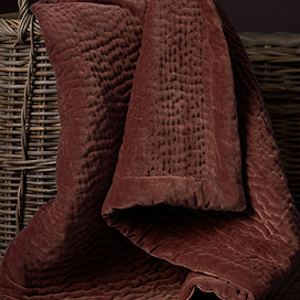close up on persimmon coloured deep velvet throw in brown whicker basket