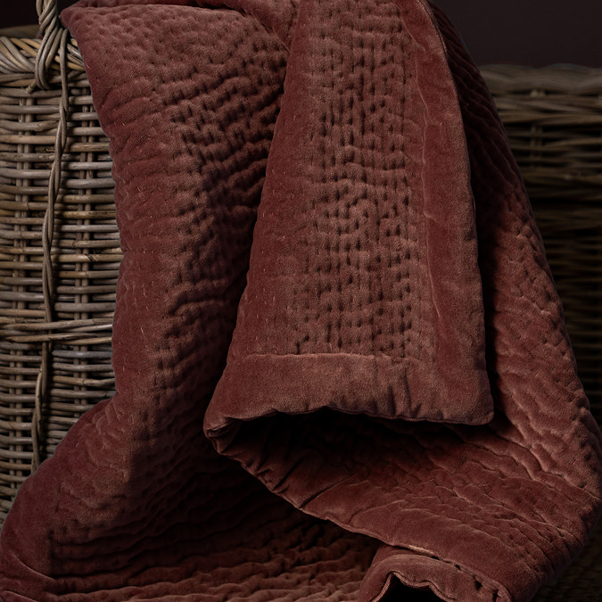 close up on persimmon coloured deep velvet throw in brown whicker basket