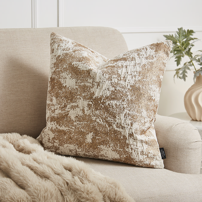 image of square gold metallic effect cushion on a cream armchair