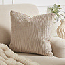 image of square natural coloured cushion with woven wavy detail on a cream armchair