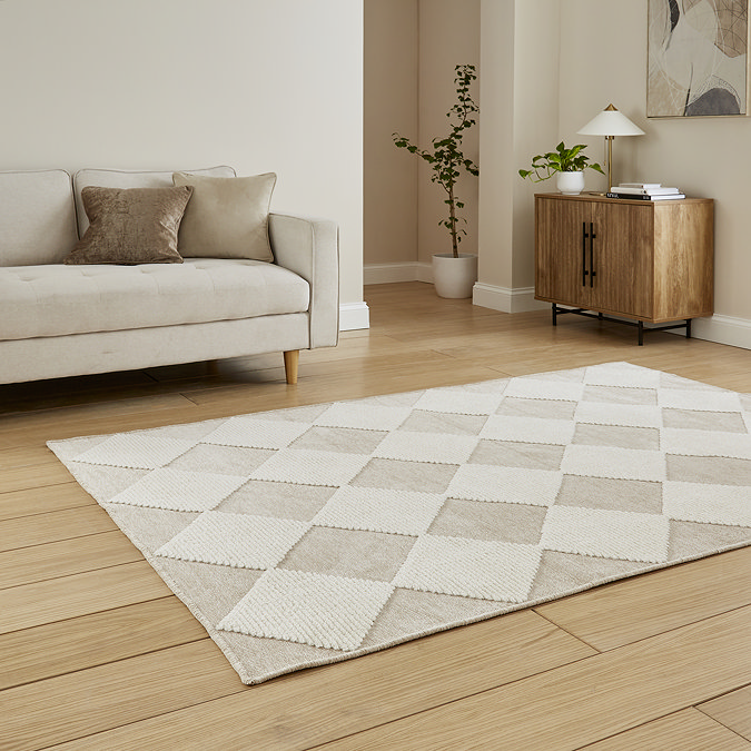 angled image of diamond checkered rug in beige and white in front of cream sofa on wooden flooring