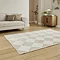 angled image of diamond checkered rug in beige and white in front of cream sofa on wooden flooring