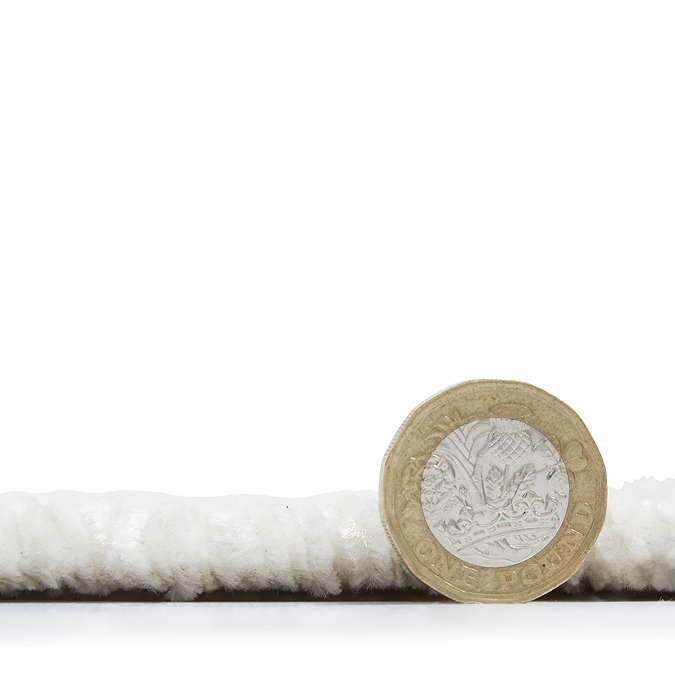 side on image of cream rug with pound coin stood next to it to show rug as half the height of coin