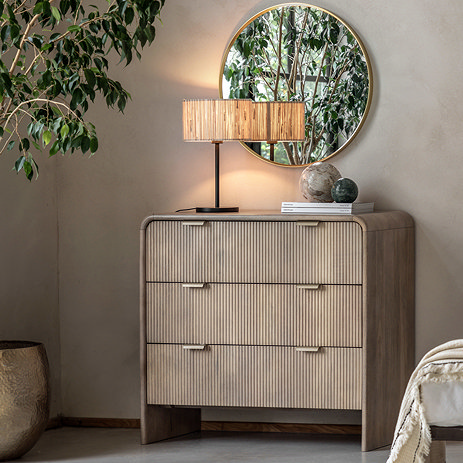 image of mango wood 3 drawer chest with smooth rounded edges and two brass handles on each drawer, with glowing lamp on top and mirror hanging over it