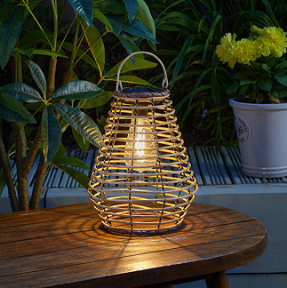 image of natural rattan outdoor lantern on wooden table, lit up at night