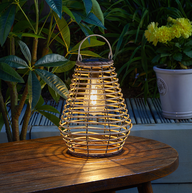 image of natural rattan outdoor lantern on wooden table, lit up at night