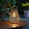 image of natural rattan outdoor lantern on wooden table, lit up at night