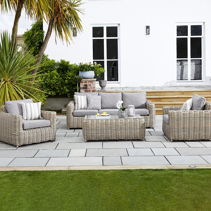 image of 3 seater rattan garden sofa with matching armchairs on either end, and glass-top rattan table in the middle, on a patio