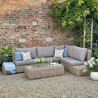 image of corner rattan sofa set, with five seats, against brick wall in garden