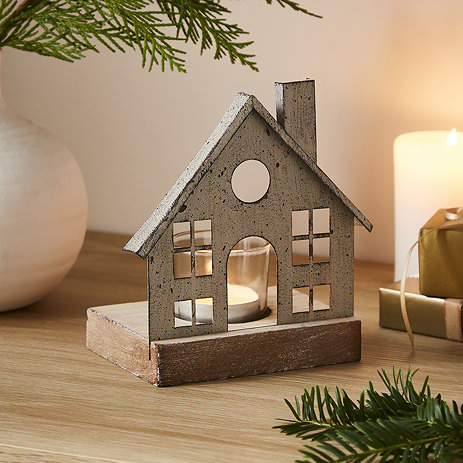 metal house tealight with glass votive, placed on a light oak sideboard and lit, surrounded by garlands, candles, and a potted plant.