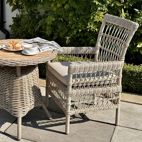 image of beige wicker dining chair with plush seat cushion next to matching bistro table, outside on patio