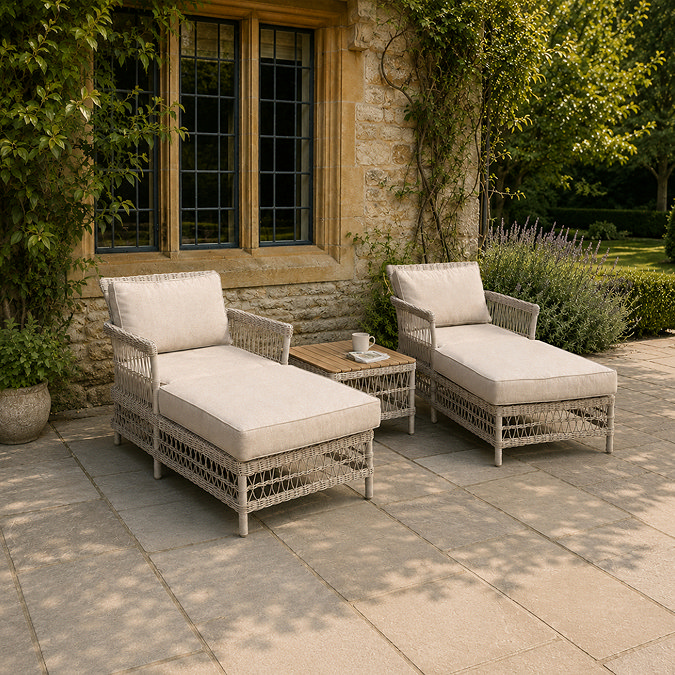 lifestyle image of two neutral wicker sun loungers outside stately house