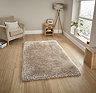 image of large beige shaggy rug in the middle of wooden flooring in front of window with beige armchair to the left