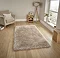 image of large beige shaggy rug in the middle of wooden flooring in front of window with beige armchair to the left