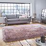 image of large pink shaggy rug in front of light grey sofa with pink accent cushions on rustic wooden floor, backlit by big apartment windows