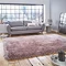 image of large pink shaggy rug in front of light grey sofa with pink accent cushions on rustic wooden floor, backlit by big apartment windows