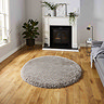 image of circular silver fluffy rug in the middle of a living room on wooden flooring, with fireplace behind and grey sofa to the right