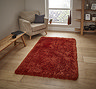 image of terracotta shaggy rug on light wooden floor next to beige armchair