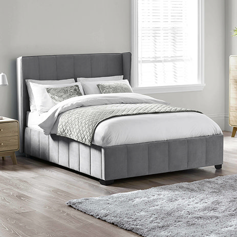 image of grey panelled velvet bedframe with subtle winged headboard, dressed in plush duvet, on wooden floor of bedroom