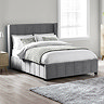 image of grey panelled velvet bedframe with subtle winged headboard, dressed in plush duvet, on wooden floor of bedroom