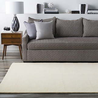 image of plain cream rug in front of grey sofa on grey wood flooring