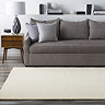 image of plain cream rug in front of grey sofa on grey wood flooring