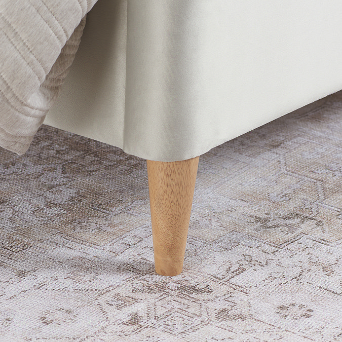 close up on wooden feet of stone coloured bedframe, resting on rug