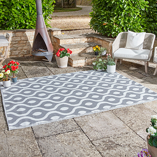 image of wavy patterned slate grey rug on stone patio next to plants and a rattan outdoor chair