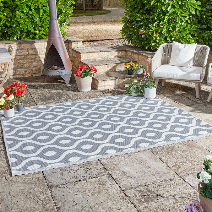 image of wavy patterned slate grey rug on stone patio next to plants and a rattan outdoor chair