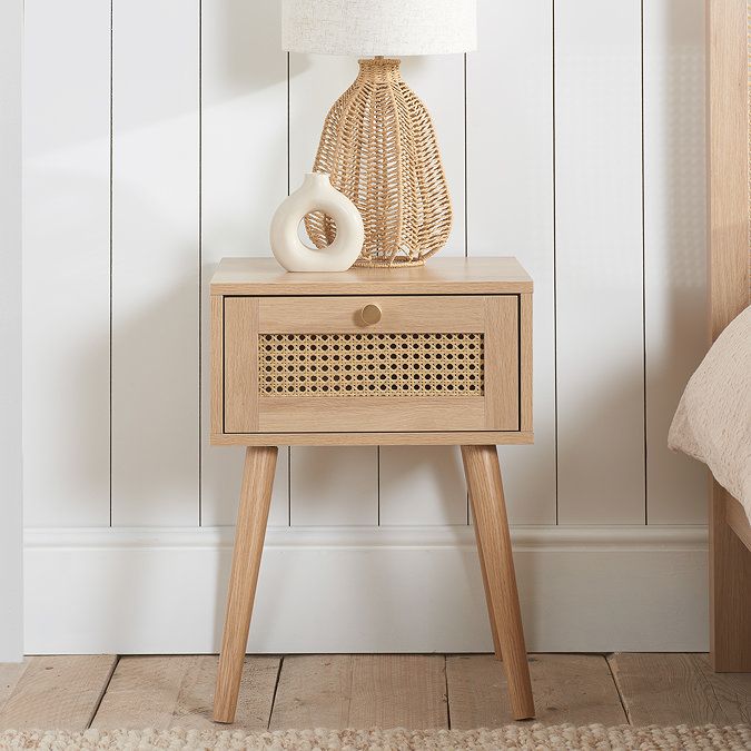 image of light oak bedside table with rattan fronted drawer, against a panelled white wall