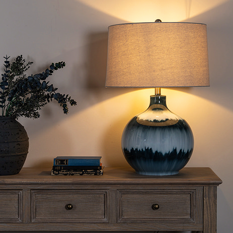 lifestyle image of an ocean blue lamp with linen shade on a sideboard