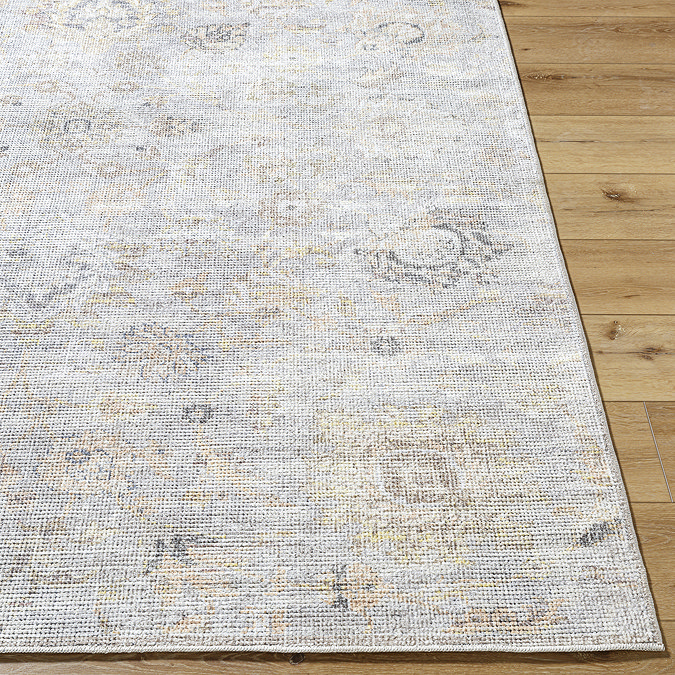 close up on corner of floral grey and beige rug on wooden flooring