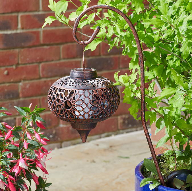 image of ornate metal lantern on a crook in daylight, highlighting its intricate floral design