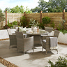 image of large rattan dining table with tempered glass top, with six matching dining chairs around it, on stone patio surrounded by brown garden fence