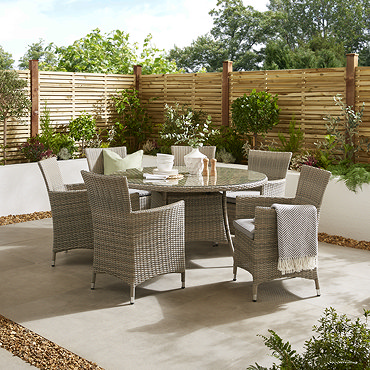 image angled from slightly above, looking over round garden table with six matching rattan chairs, on a stone patio