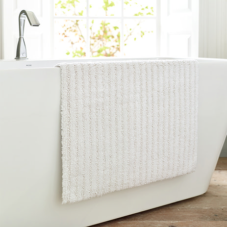 image of soft white bath mat draped over the side of a ceramic bath