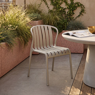 image of putty coloured plastic chair with slatted back and no arms, on patio next to round modern concrete cream table