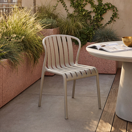 image of putty coloured plastic chair with slatted back and no arms, on patio next to round modern concrete cream table